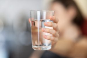 Frau hält Glas mit Leitungswasser ins Bild