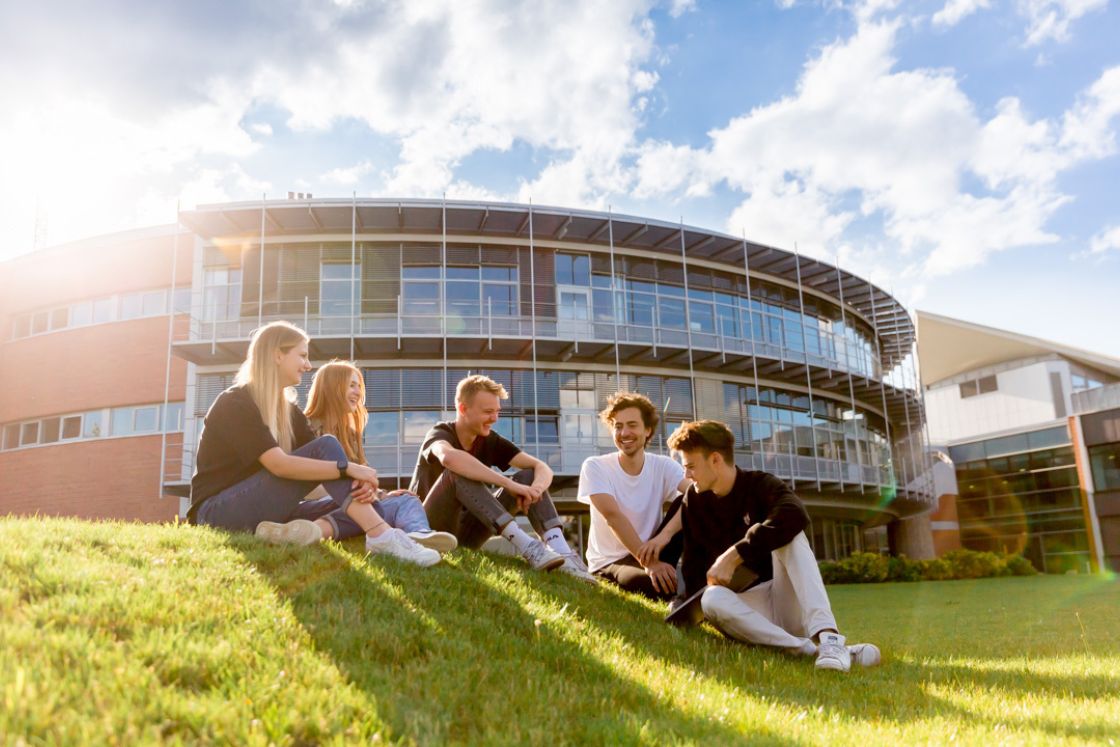 Studierende sitzen vor einem Gebäude auf der Wiese