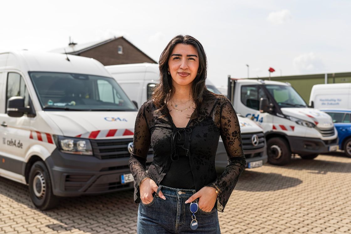 Junge Frau steht vor Firmenfahrzeugen.