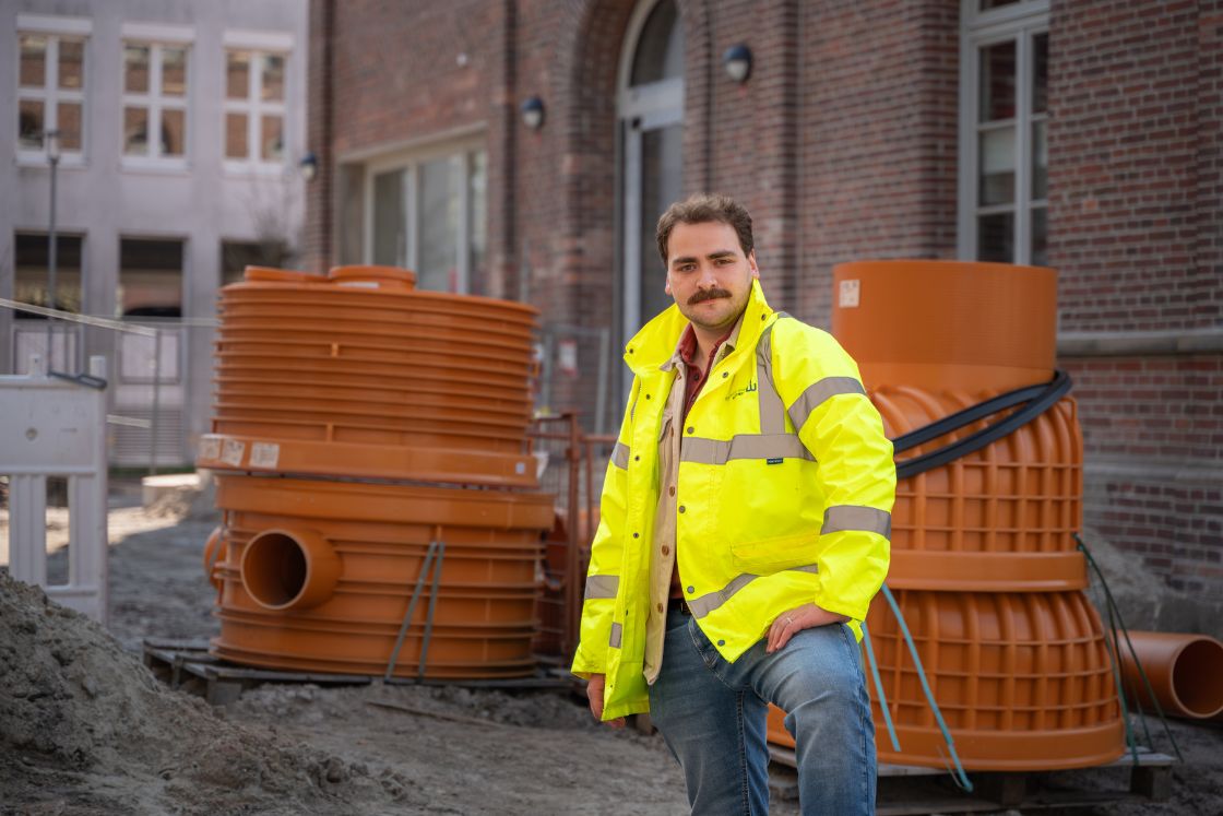 Junger Mann steht in Arbeitsjacke auf einer Baustelle.
