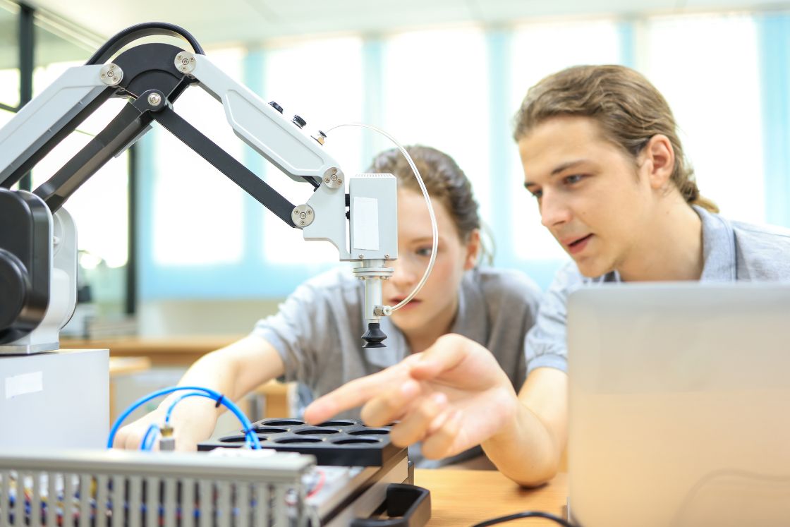 Zwei Studierende testen und inspizieren einen mechanischen Greifarm
